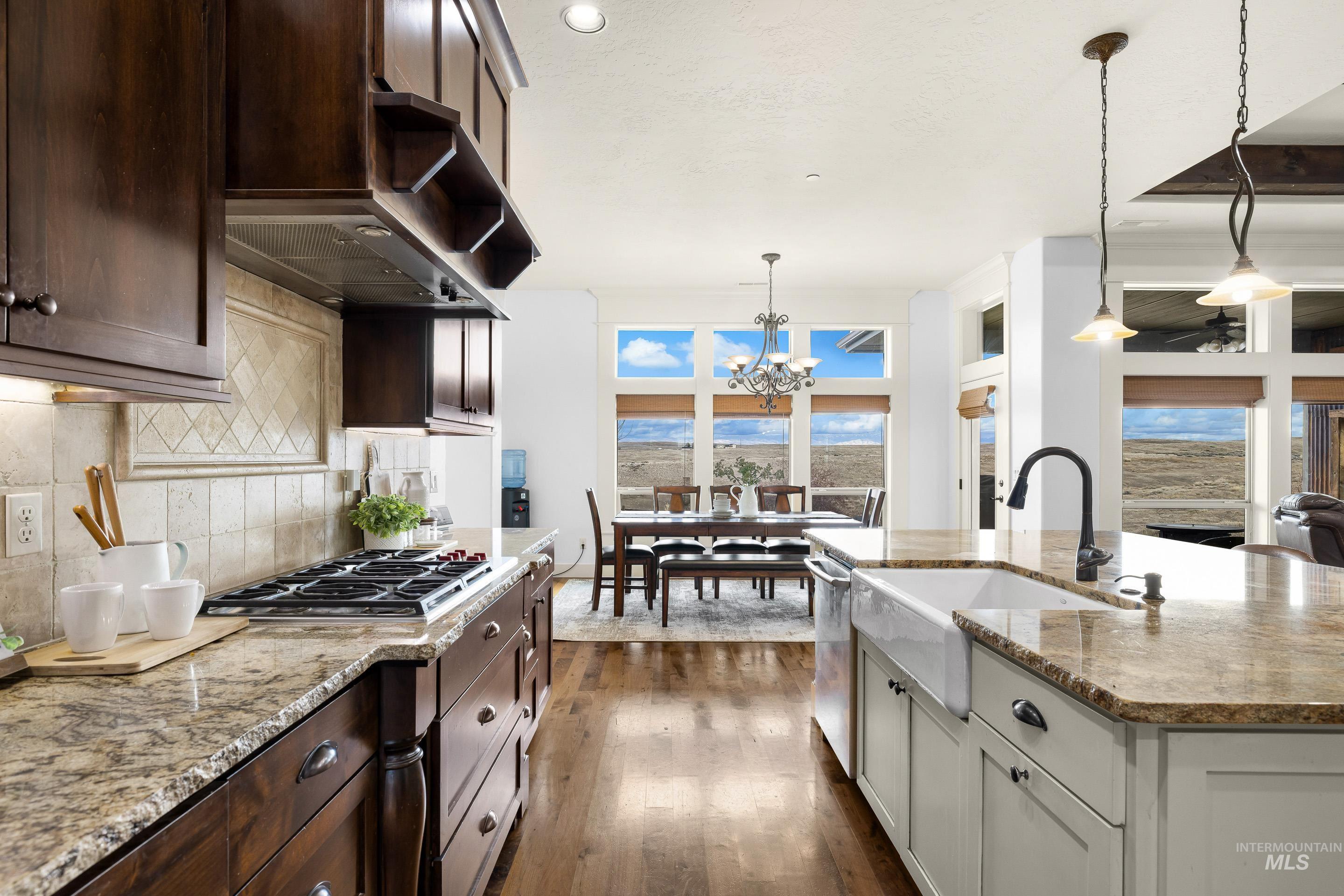 7521 North Grand Ridge Lane Eagle, ID 83616 - Photo 20 of 50 Kitchen featuring light stone counters, dark wood-style flooring, decorative backsplash, suspended lighting, and plenty of natural light