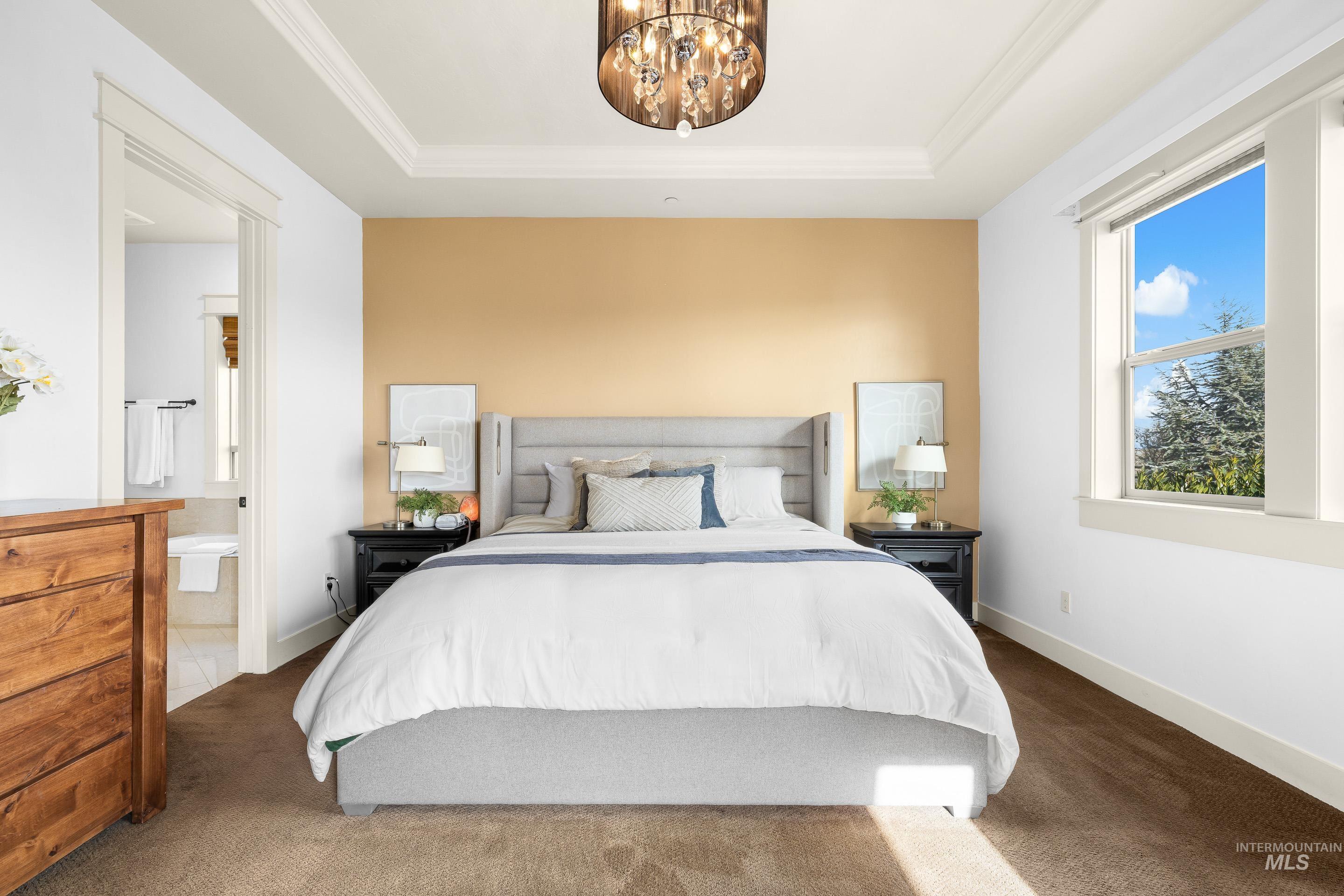 7521 North Grand Ridge Lane Eagle, ID 83616 - Photo 27 of 50 Carpeted bedroom featuring a tray ceiling, hanging lights, ornamental molding, and connected bathroom
