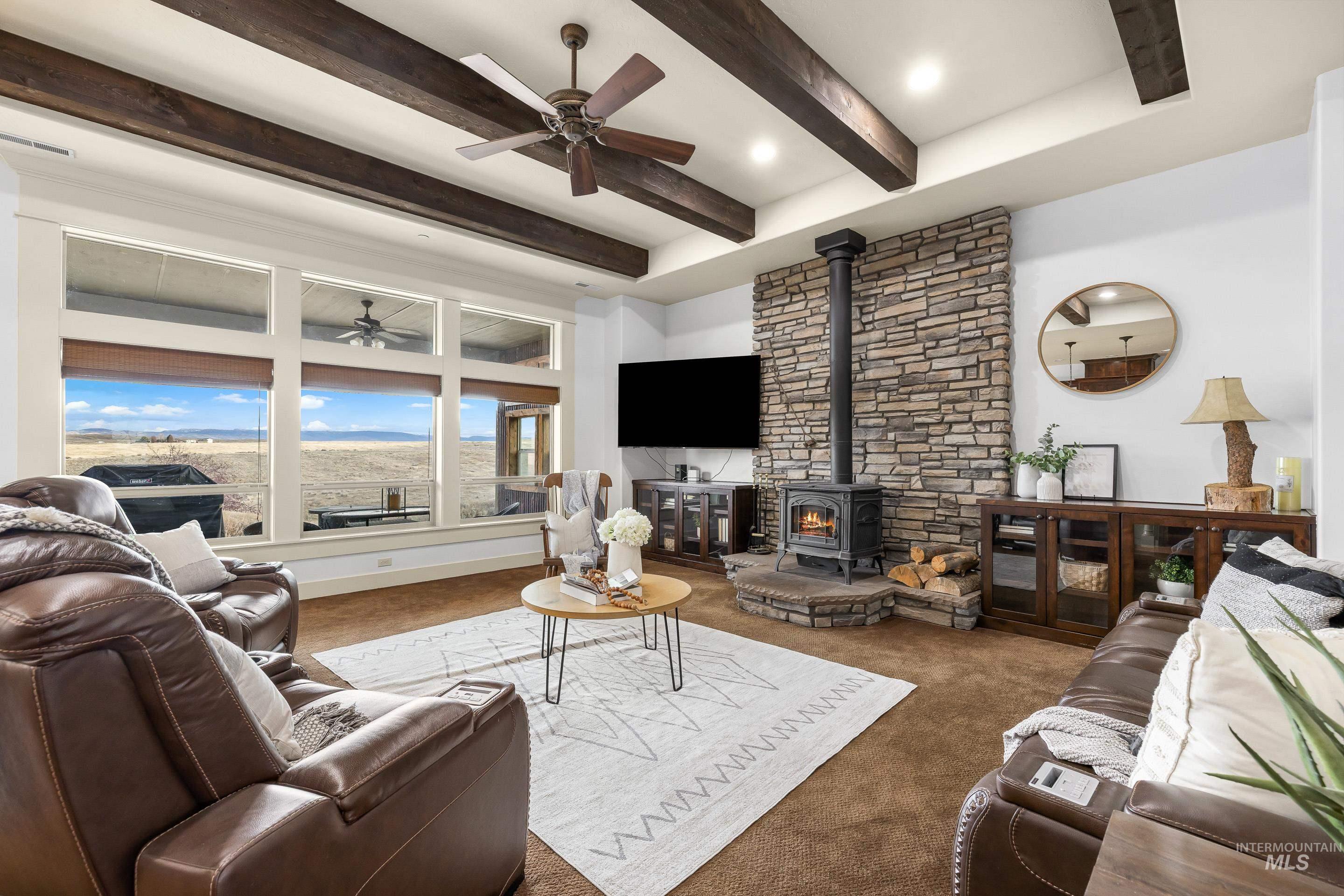 7521 North Grand Ridge Lane Eagle, ID 83616 - Photo 10 of 50 Carpeted living area with ceiling fan, a wood stove, and beamed ceiling