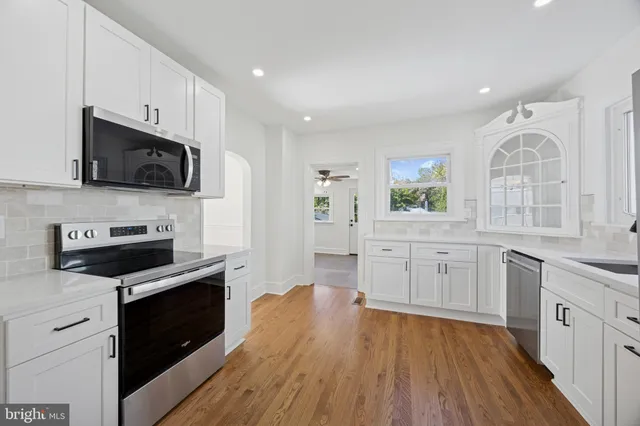 a kitchen with stainless steel appliances white cabinets a sink a stove a microwave and wooden floors
