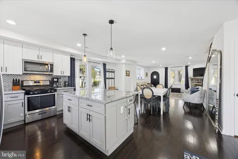 a kitchen with stainless steel appliances kitchen island granite countertop a stove top oven a sink a dining table and chairs with wooden floor