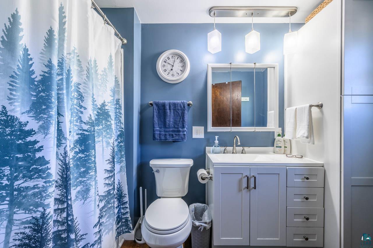 2581 O'Rourke Road Hibbing, MN 55746 - Photo 14 of 61 Bathroom featuring a light blue vanity with a white countertop and integrated sink, a wall-mounted medicine cabinet with a mirror, and a white toilet
