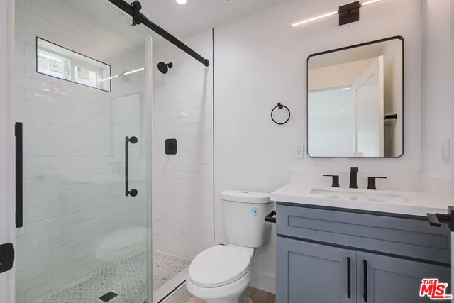 a bathroom with a toilet a sink a glass door a shower a mirror and vanity