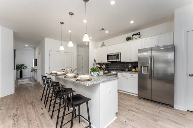 a kitchen with stainless steel appliances kitchen island granite countertop a refrigerator a stove a sink a dining table and chairs with wooden floor