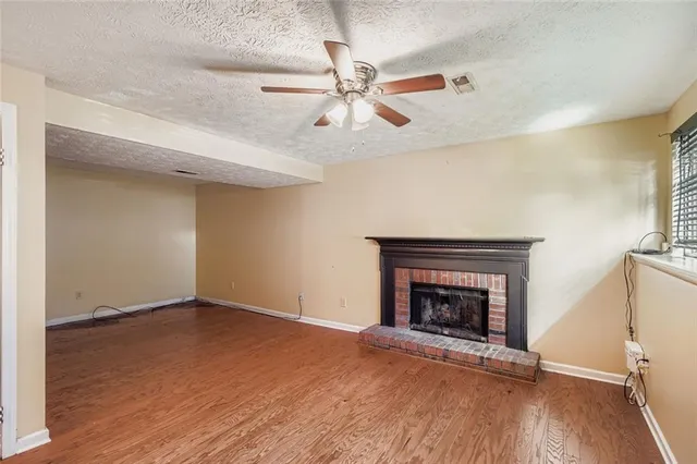 an empty room with wooden floor a ceiling fan a fireplace and windows