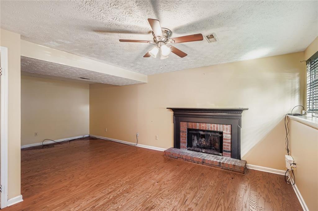 6134 Raintree Bend Lithonia, GA 30058 - Photo 15 of 17 an empty room with wooden floor a ceiling fan a fireplace and windows