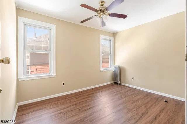 an empty room with wooden floor fan and windows