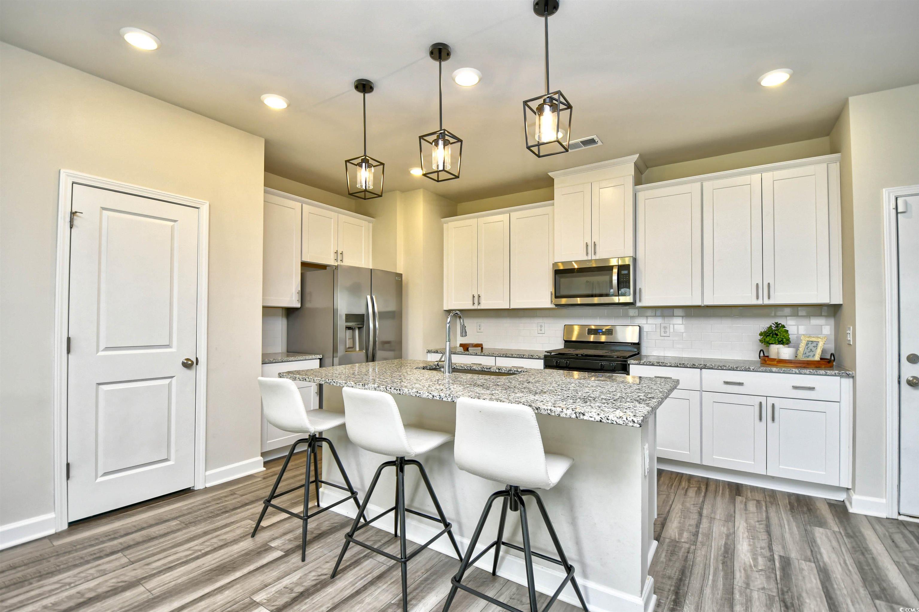 2325 Copper Crk Loop Longs, SC 29568 - Photo 11 of 40 Kitchen featuring white cabinets, a breakfast bar, light stone countertops, appliances with stainless steel finishes, and pendant lighting