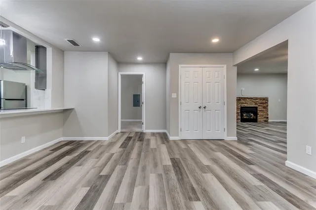 a view of empty room with wooden floor and kitchen