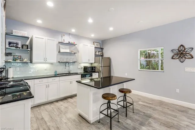 a kitchen with stainless steel appliances granite countertop a stove top oven a sink a dining table and chairs with wooden floor