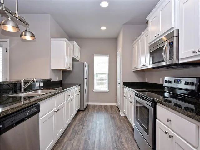 a kitchen with stainless steel appliances granite countertop a stove a sink dishwasher and white cabinets with wooden floor