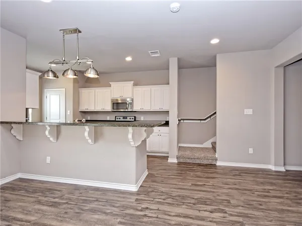 a view of a kitchen with stainless steel appliances granite countertop a refrigerator a sink dishwasher a stove and a dining table with wooden floor