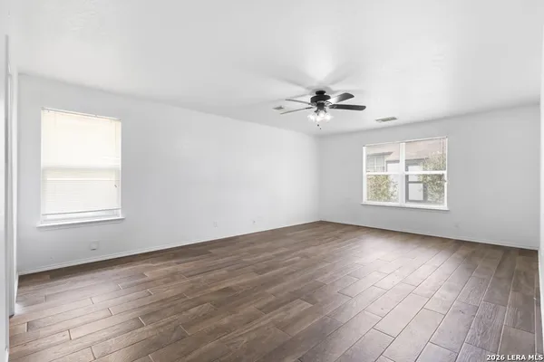 an empty room with wooden floor chandelier fan and windows
