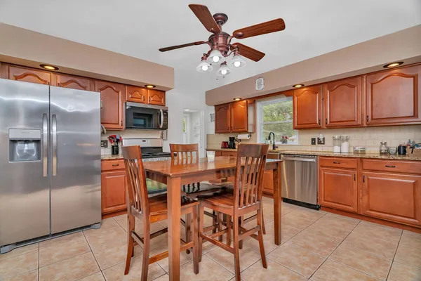 a kitchen with stainless steel appliances kitchen island granite countertop a refrigerator a stove a sink a dining table and chairs with wooden floor