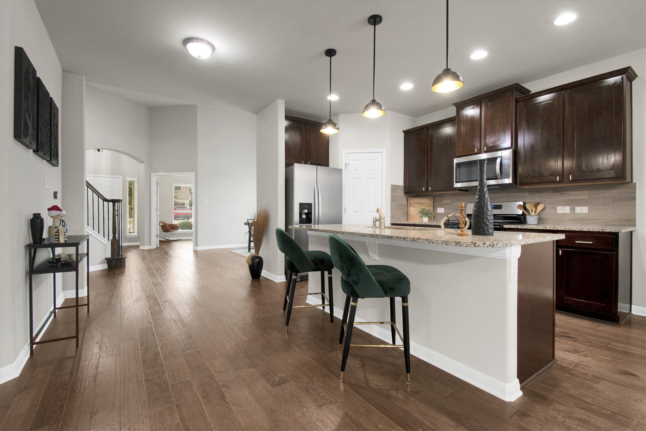 Kitchen with a kitchen bar, dark brown cabinetry, an island with sink, hanging light fixtures, and light stone counters