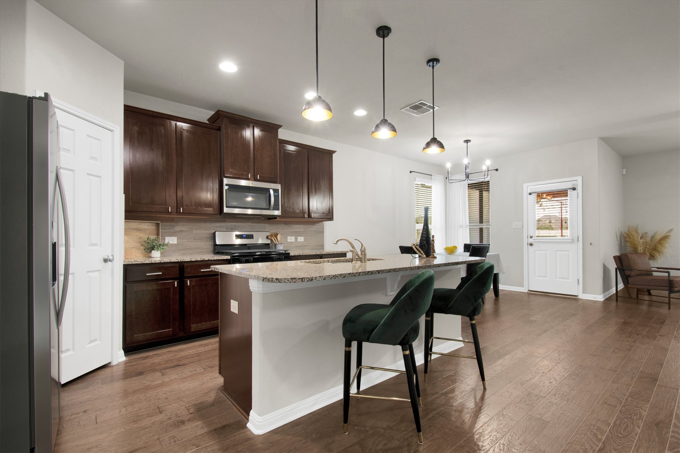 13601 Larrys Lane Manchaca, TX 78652 - Photo 8 of 40 Kitchen featuring appliances with stainless steel finishes, pendant lighting, decorative backsplash, a kitchen island with sink, and dark brown cabinetry