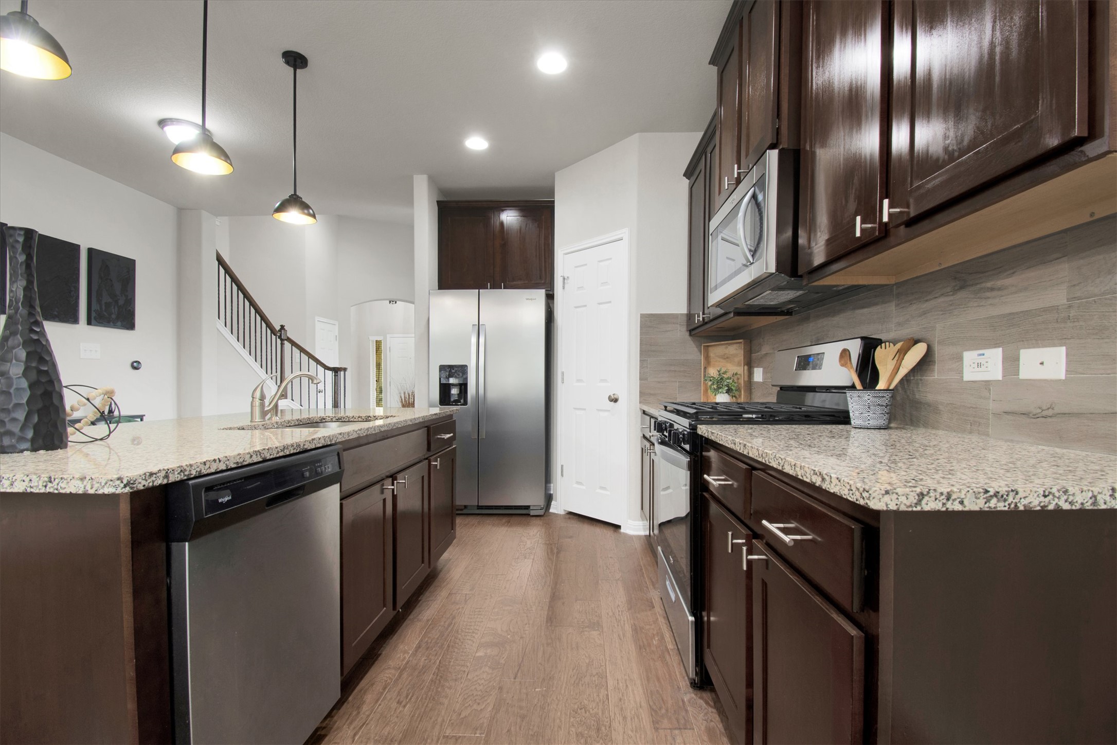 13601 Larrys Lane Manchaca, TX 78652 - Photo 9 of 40 Kitchen featuring dark brown cabinets, stainless steel appliances, light wood-type flooring, light stone counters, and decorative light fixtures