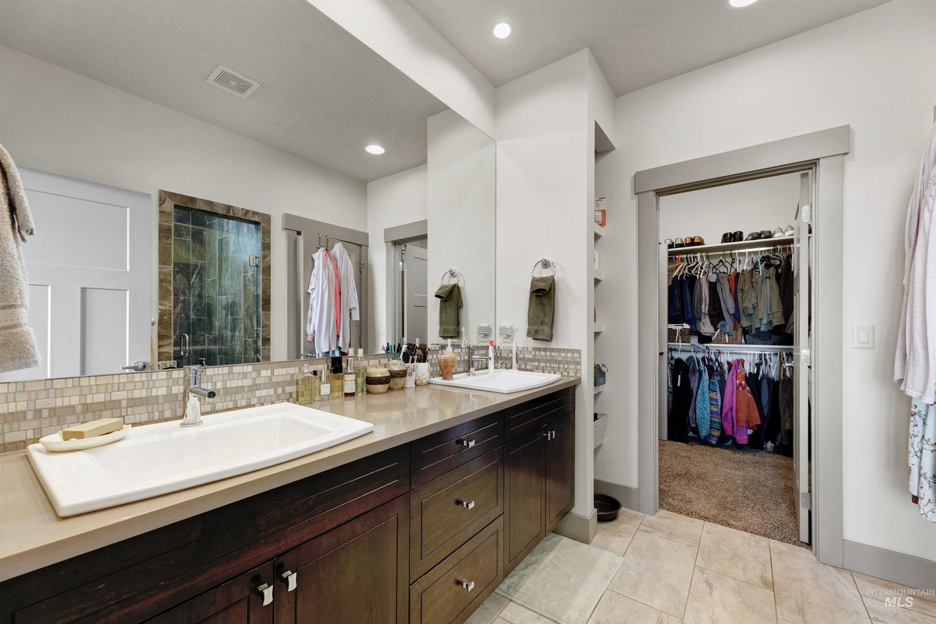 24398 Tombstone Ridge Court Middleton, ID 83644 - Photo 17 of 47 Bathroom featuring a dual vanity with rectangular sinks, wood-finish cabinetry, and a textured tile backsplash