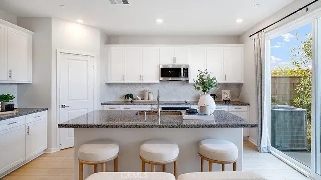 a kitchen with stainless steel appliances granite countertop a stove a sink a microwave a refrigerator and white cabinets with wooden floor