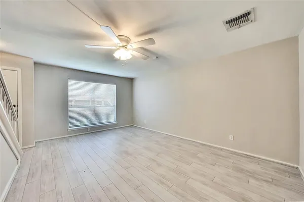 an empty room with wooden floor fan and windows