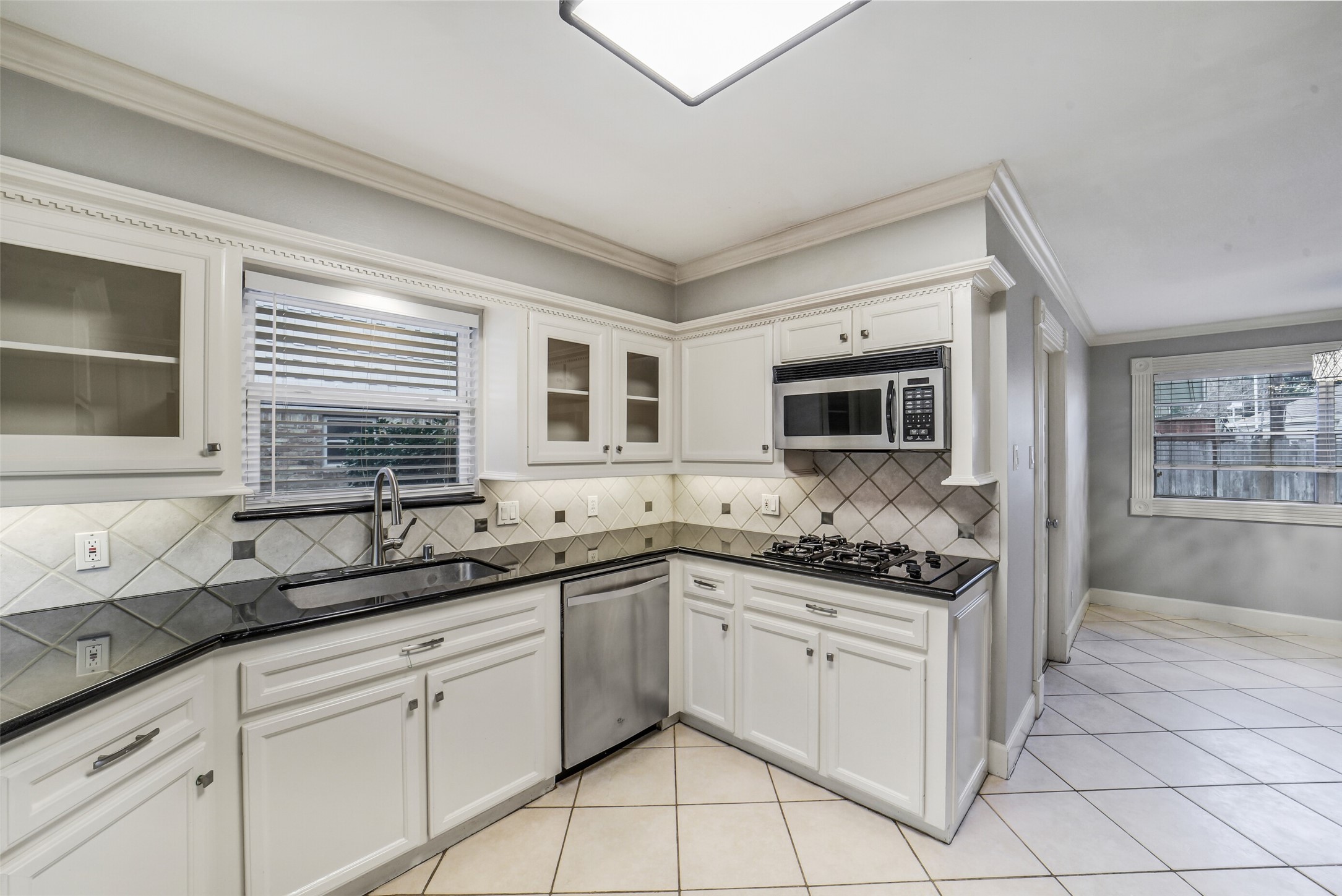 5322 Rutherglenn Drive Houston, TX 77096 - Photo 12 of 30 Bright, updated kitchen featuring white cabinetry with glass-front window cabinets, tile backsplash and under cabinet lighting.