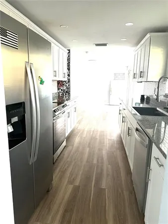 a kitchen with stainless steel appliances granite countertop a refrigerator a sink dishwasher a stove and white countertops with wooden floor