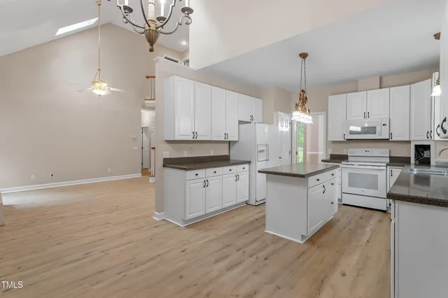 a kitchen with stainless steel appliances white cabinets a sink a stove a refrigerator and island with wooden floor