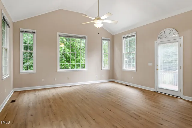 an empty room with wooden floor chandelier fan and windows