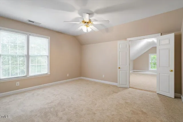 an empty room with chandelier fan and windows