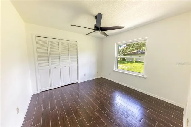 an empty room with wooden floor chandelier fan and windows