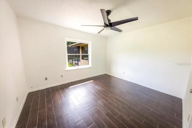 an empty room with wooden floor ceiling fan and windows