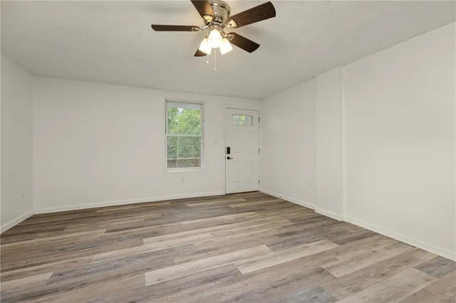 an empty room with wooden floor chandelier fan and windows