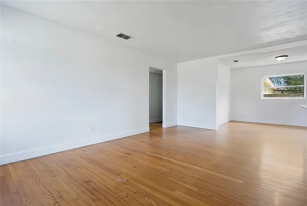 a view of an empty room with wooden floor and a window