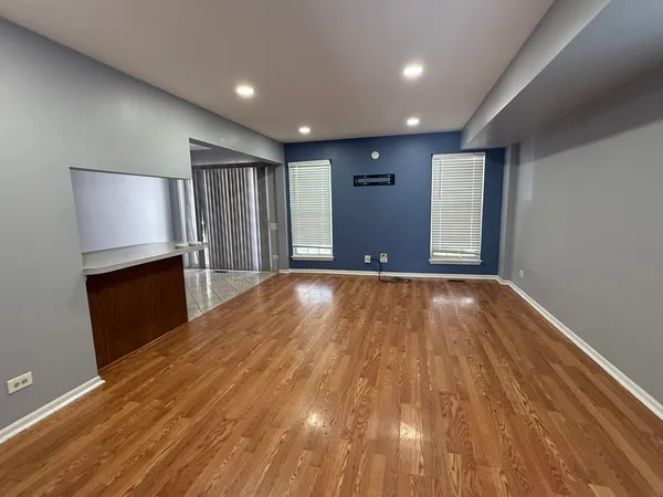 a view of an empty room with wooden floor and a kitchen