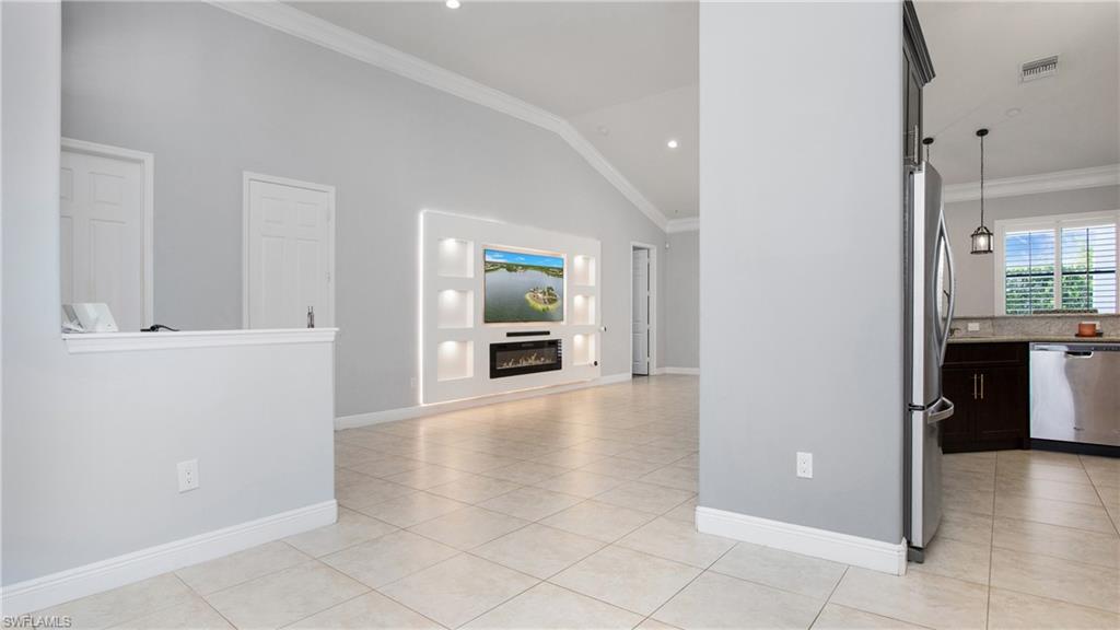 6341 Green Boulevard Naples, FL 34116 - Photo 21 of 48 Unfurnished living room featuring light tile patterned flooring, crown molding, baseboards, a glass covered fireplace, and high vaulted ceiling
