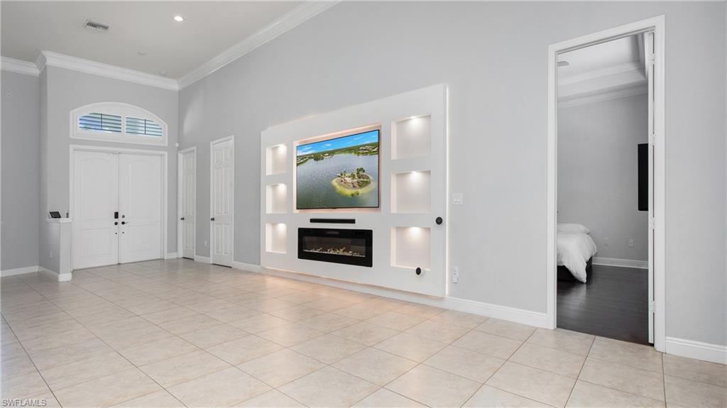 6341 Green Boulevard Naples, FL 34116 - Photo 24 of 48 Foyer featuring crown molding, light tile patterned flooring, baseboards, a glass covered fireplace, and a towering ceiling
