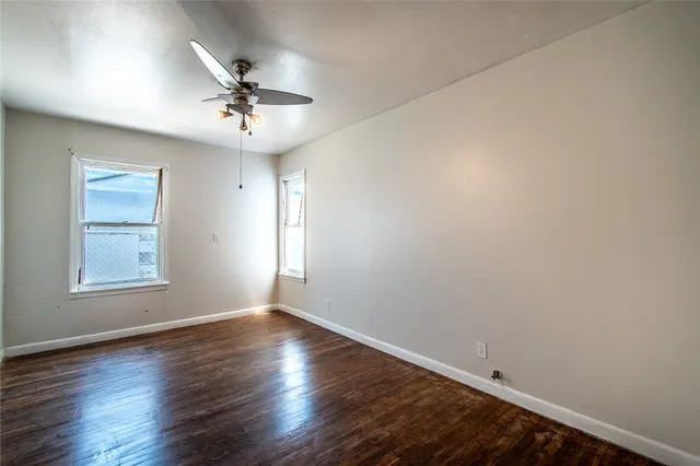 an empty room with wooden floor chandelier fan and windows