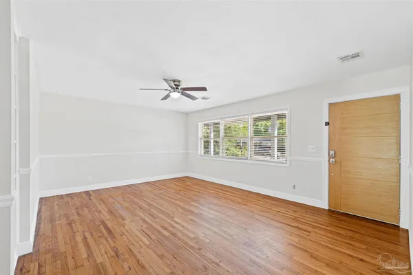 an empty room with wooden floor chandelier fan and windows