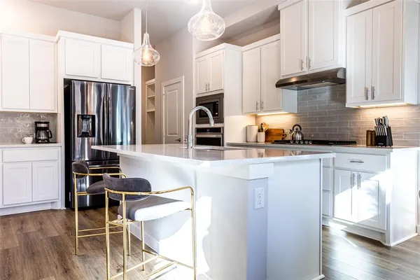 a kitchen with stainless steel appliances a stove a refrigerator a sink a dining table and chairs with wooden floor