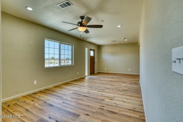 an empty room with wooden floor fan and windows