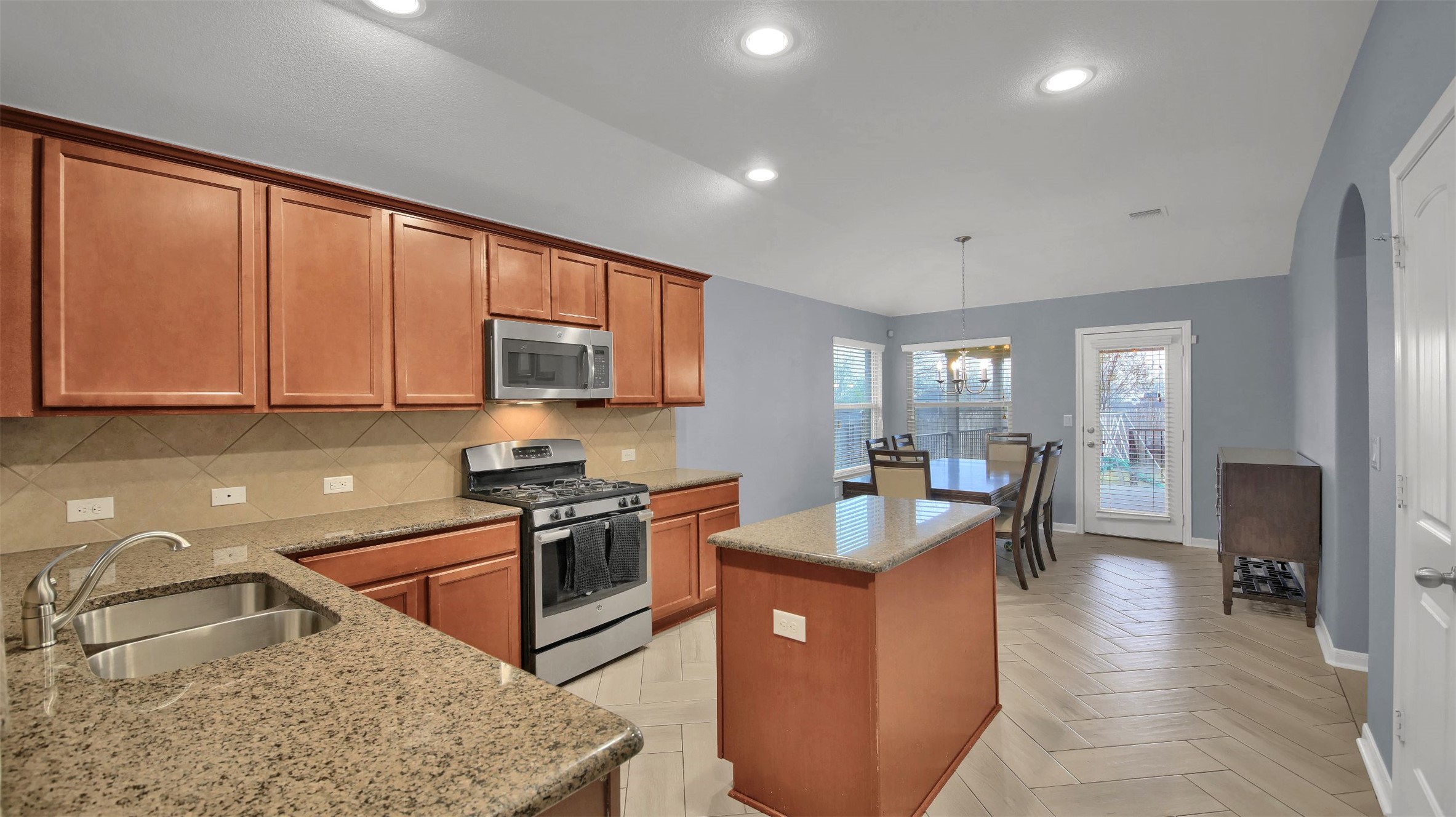 18005 Moreto Loop Pflugerville, TX 78660 - Photo 6 of 25 Kitchen featuring appliances with stainless steel finishes, brown cabinets, decorative backsplash, a kitchen island, and recessed lighting