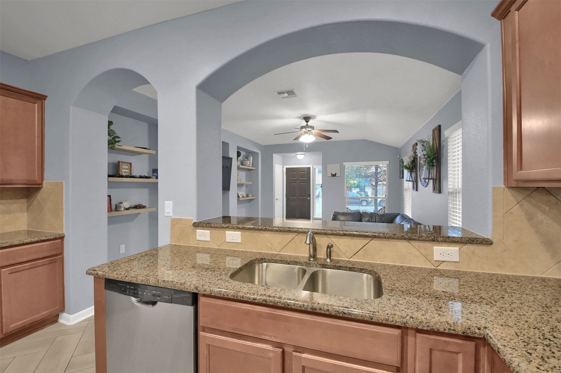 18005 Moreto Loop Pflugerville, TX 78660 - Photo 8 of 25 Kitchen with backsplash, brown cabinets, light stone countertops, dishwasher, and arched walkways