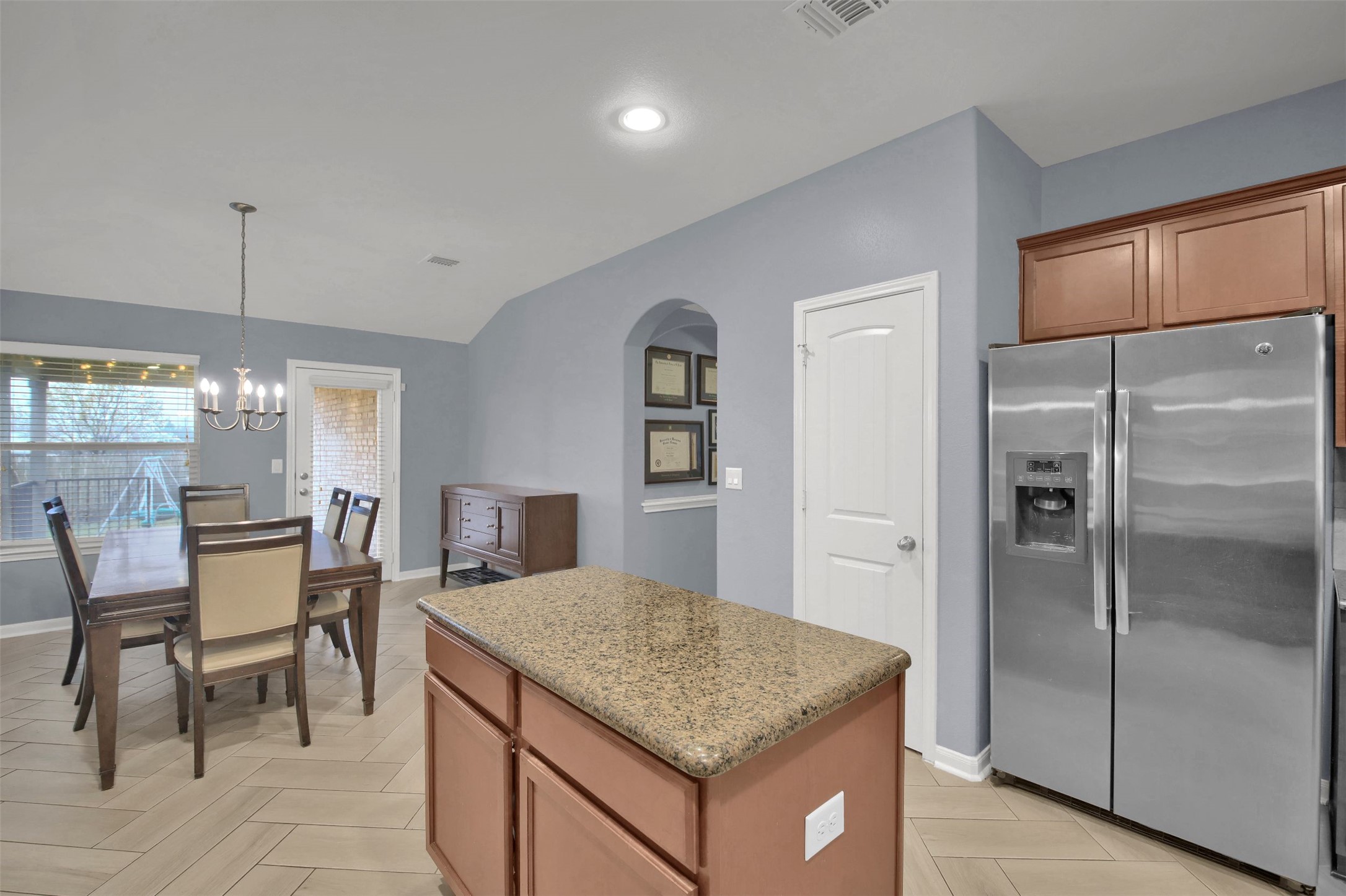 18005 Moreto Loop Pflugerville, TX 78660 - Photo 9 of 25 Kitchen featuring stainless steel refrigerator with ice dispenser, a kitchen island, decorative light fixtures, brown cabinetry, and vaulted ceiling