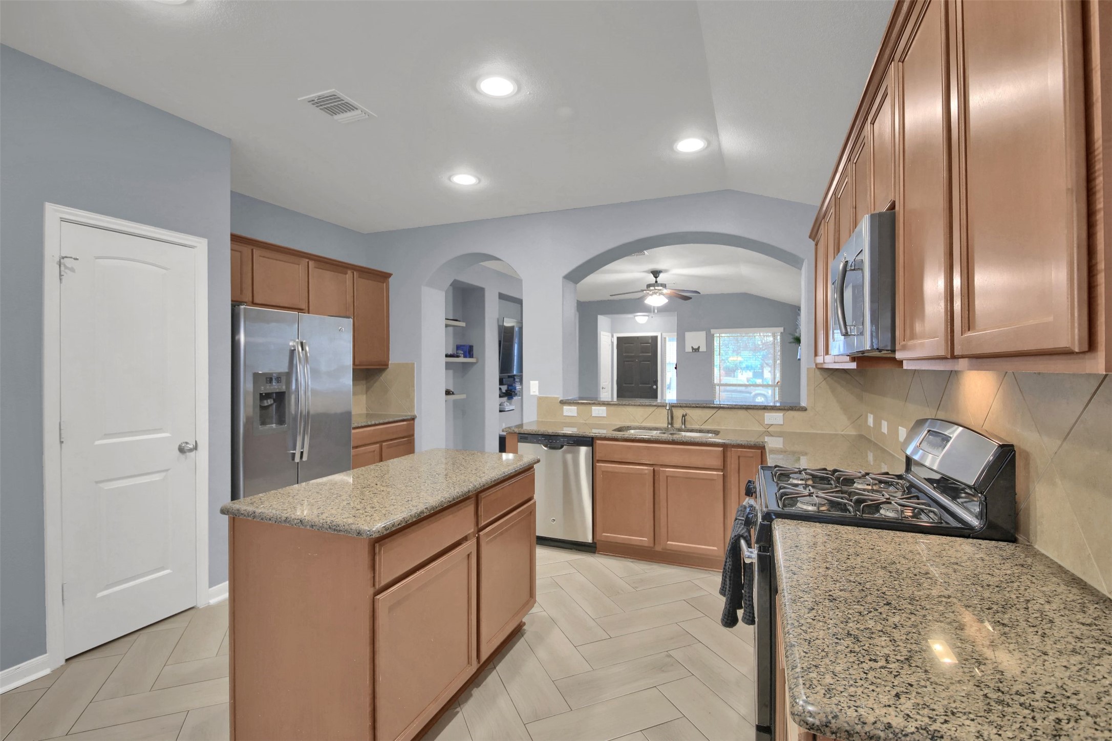18005 Moreto Loop Pflugerville, TX 78660 - Photo 10 of 25 Kitchen featuring appliances with stainless steel finishes, a kitchen island, light stone countertops, a ceiling fan, and brown cabinetry