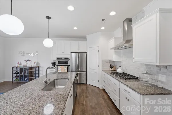 a kitchen with granite countertop a stove a sink a refrigerator island wooden floor and chairs