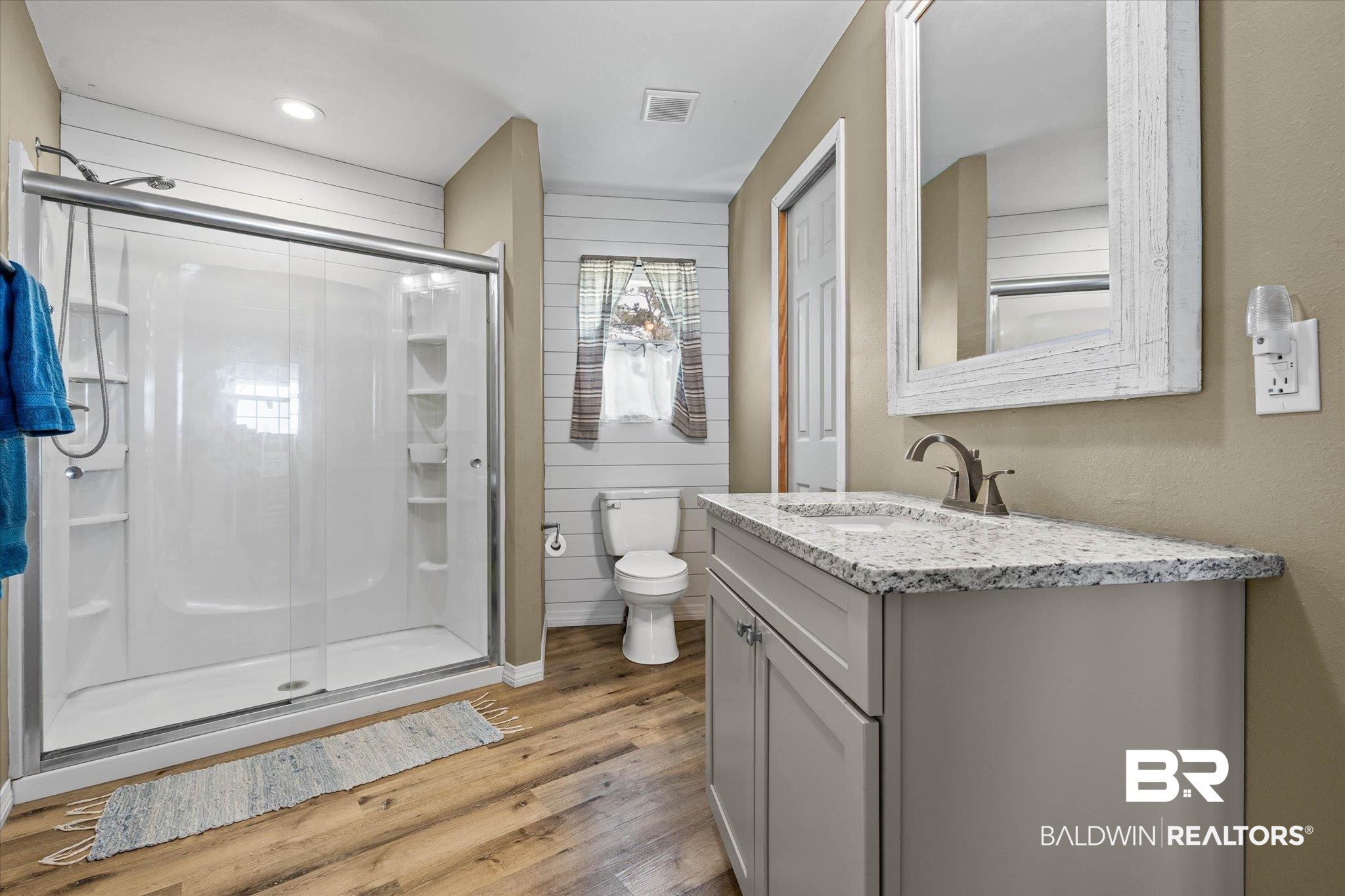 9100 Shell Belt Road Coden, AL 36523 - Photo 13 of 38 Bathroom featuring a single vanity with a granite countertop and brushed nickel faucet, a white shower enclosure with sliding glass doors, wood-finish flooring, and white horizontal paneling