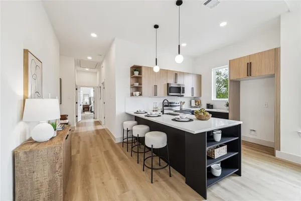 a kitchen with stainless steel appliances a stove a sink a refrigerator white cabinets and couches with wooden floor