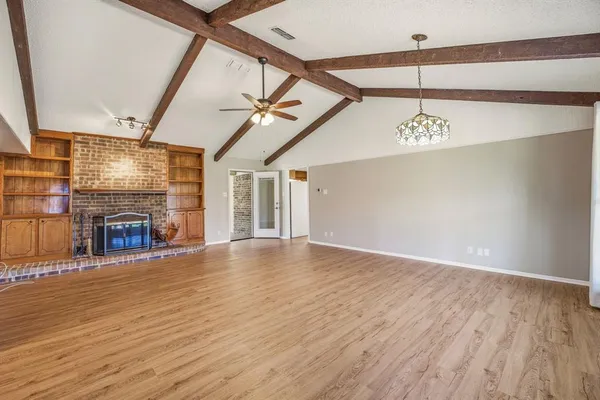 a view of an empty room with wooden floor fireplace and a window