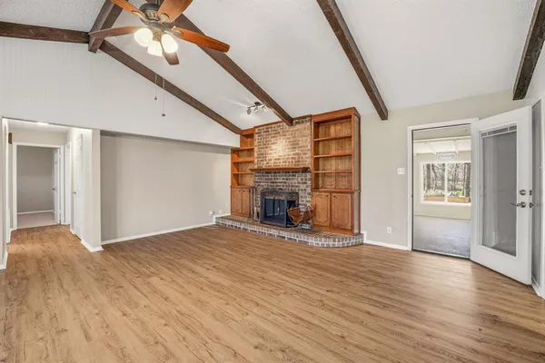 a view of an empty room with wooden floor fireplace and a window