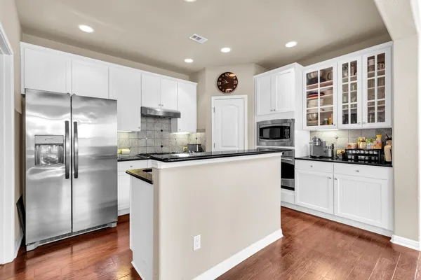 a kitchen with stainless steel appliances granite countertop a refrigerator a oven a sink and white cabinets with wooden floor